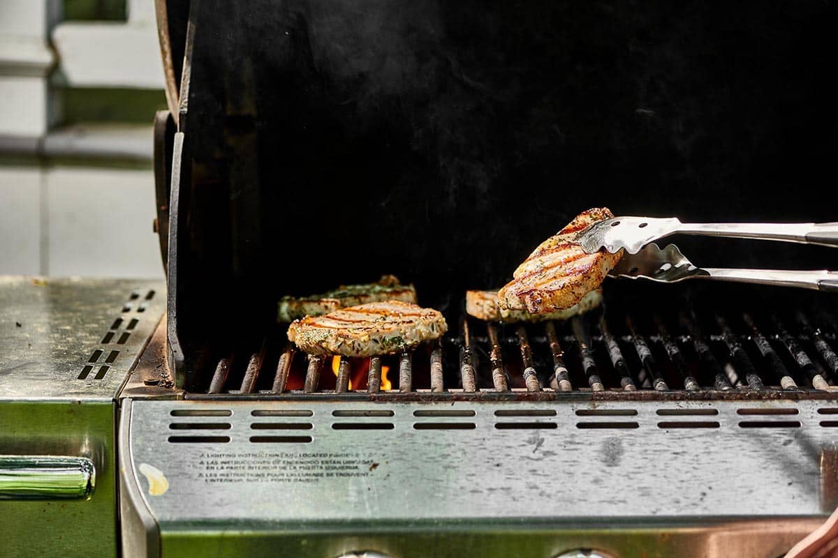 Grilling pork chops and flipping with tongs.