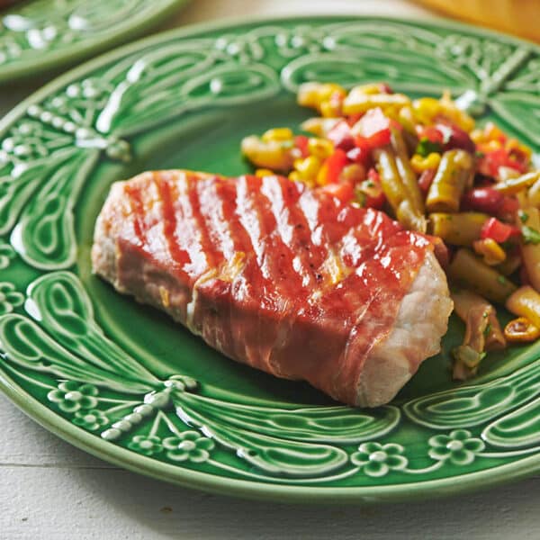 Grilled Prosciutto Wrapped Pork Chops on green plate with vegetables.