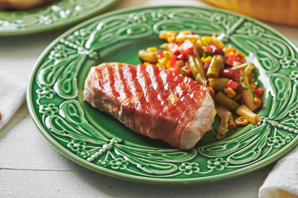 Grilled Prosciutto Wrapped Pork Chops on green plate with vegetables.