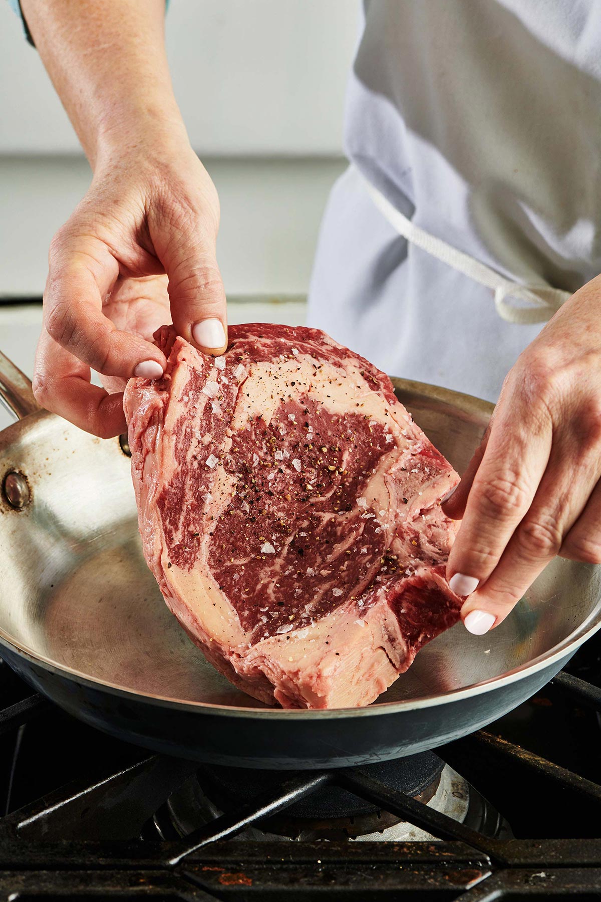Woman placing raw ribeye into pan on stovetop.