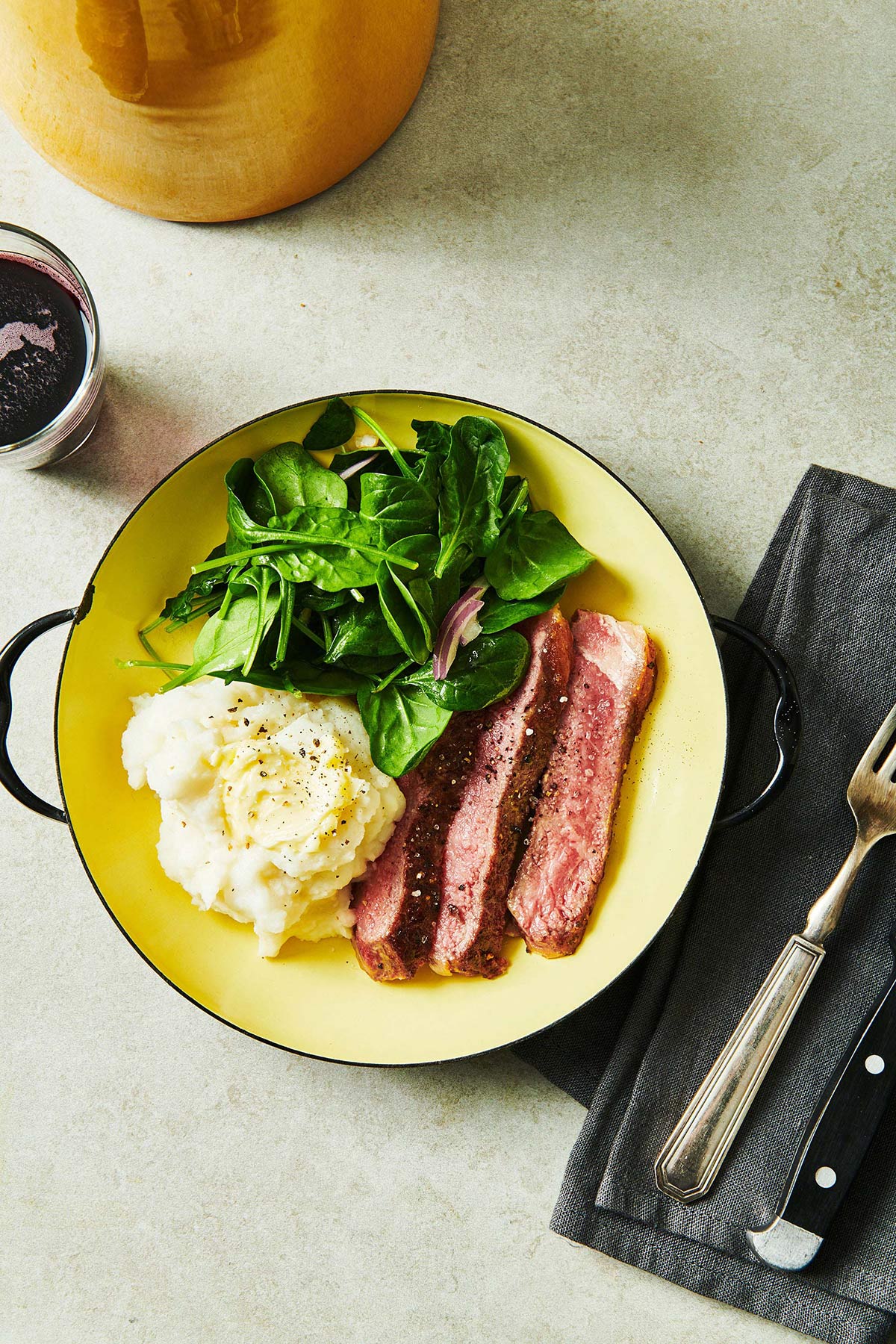 Sliced ribeye on plate with mashed potatoes and salad.