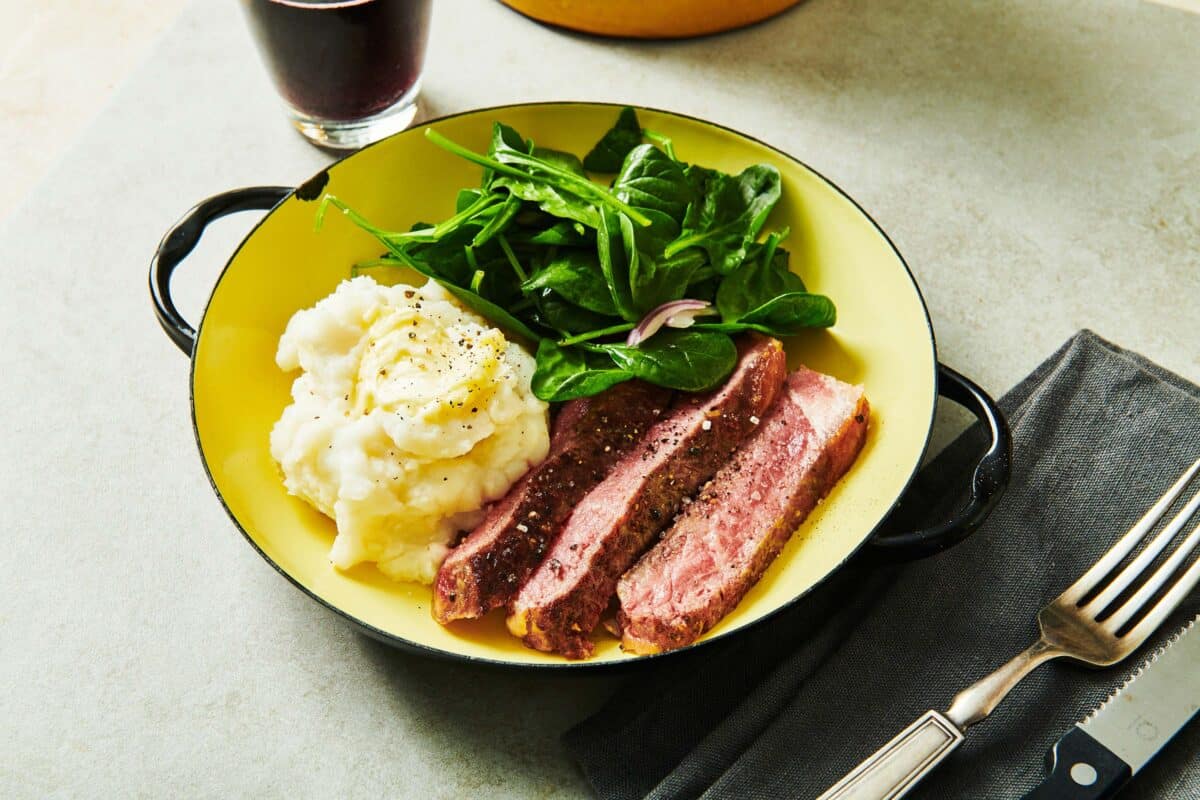 Pan-seared ribeye on plate with mashed potatoes and salad.