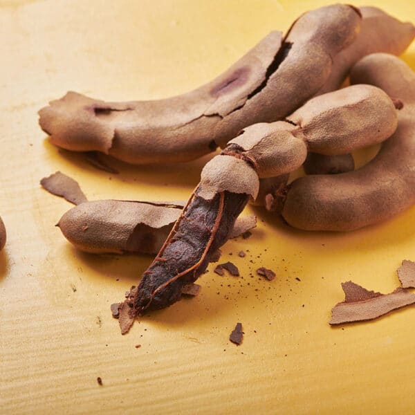 Whole and broken tamarind pods on yellow table.
