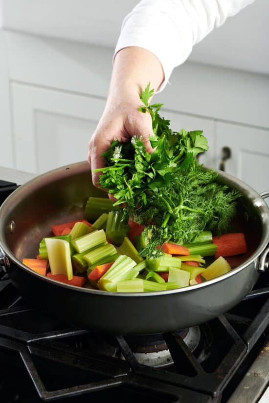 Person adding a handful of herbs to a pan of vegetables.