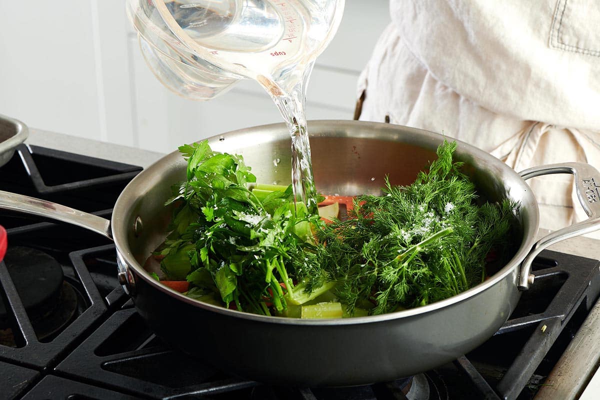 Water pouring over a pan of herbs and vegetables.