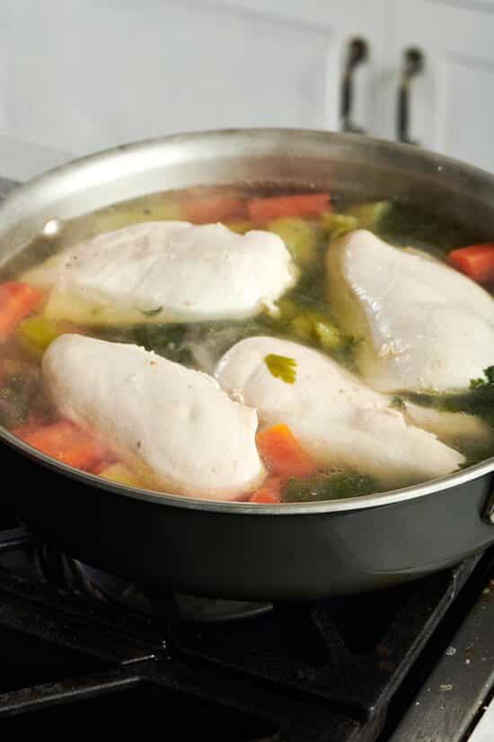 Chicken in a pan with water and vegetables.