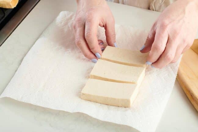 Woman arranging tofu slices on a paper towel.