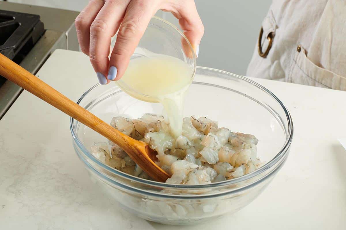 Woman pouring lime juice onto shrimp in a bowl.