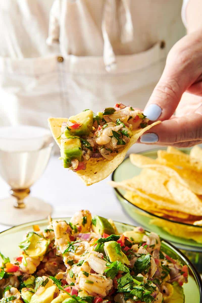 Woman holding tortilla chip loaded with colorful Shrimp Ceviche.