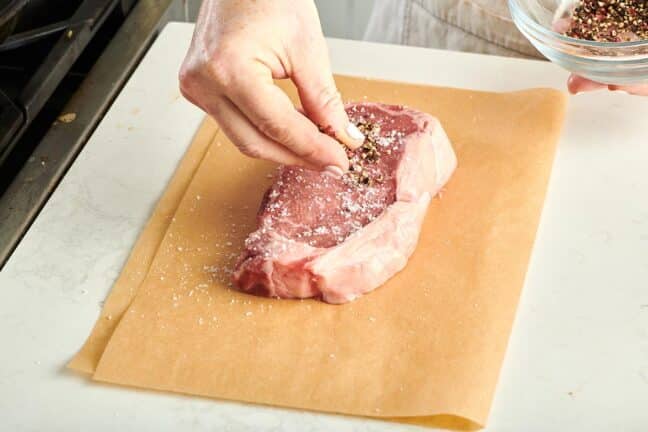 Woman seasoning a NY strip steak on parchment paper.
