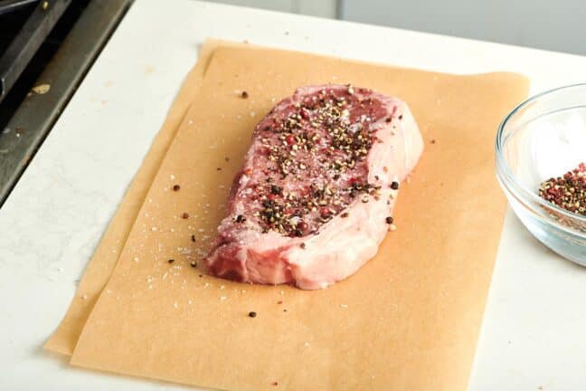 NY strip steam topped with pepper on parchment paper.