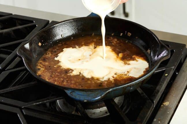 Cream pouring into a pan of brown sauce.