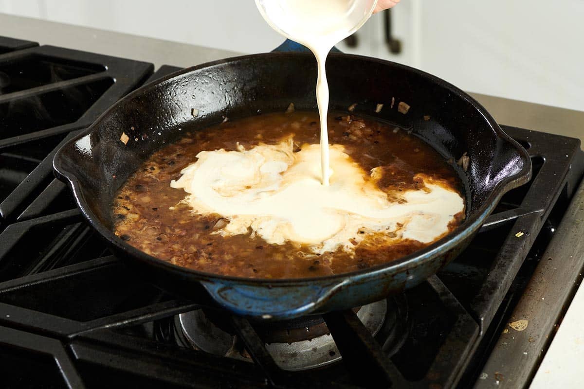 Cream pouring into a pan of brown sauce.