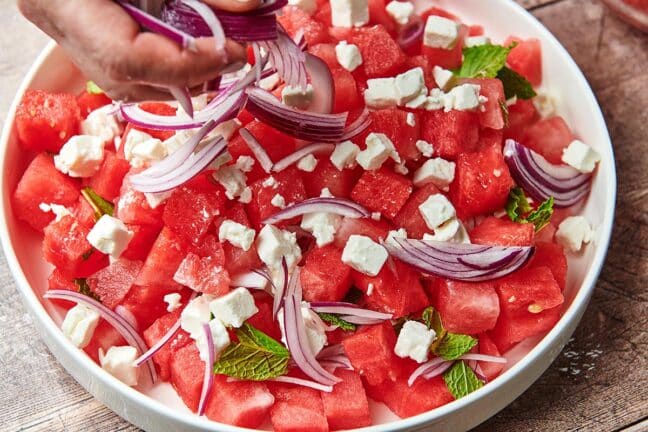Woman putting red onion onto watermelon and feta.