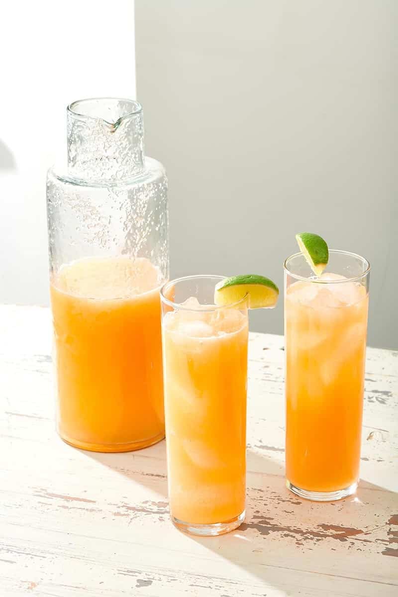 Two glasses and a pitcher of orange-colored Agua Fresca.