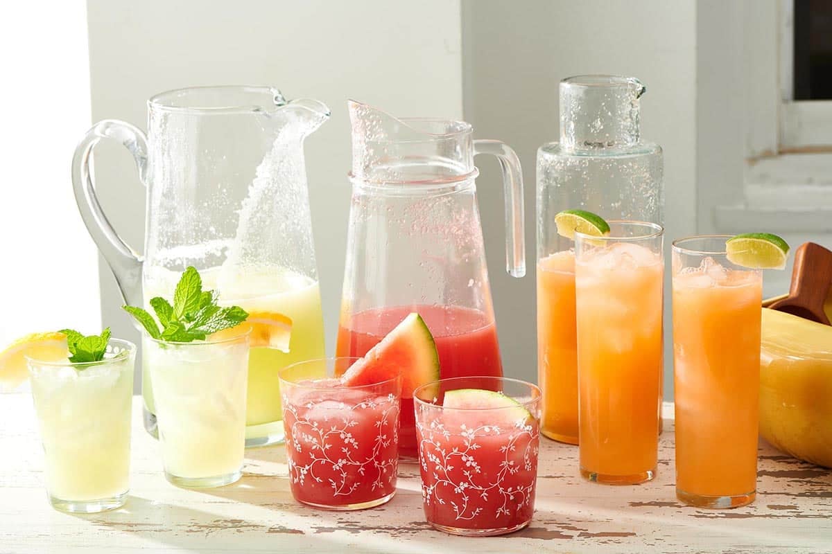 Orange, red, and yellow agua fresca in various glass containers.