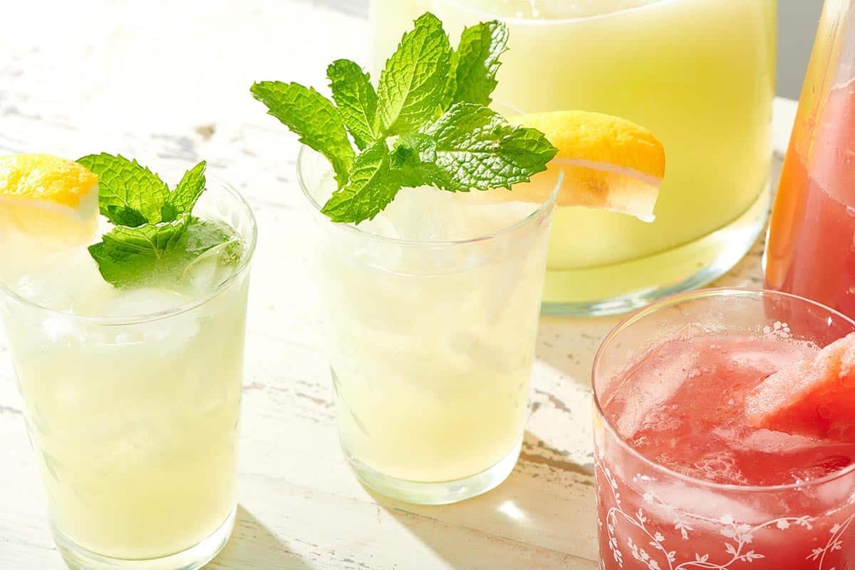Glasses of Agua Fresca topped with mint leaves and lemon wedges.