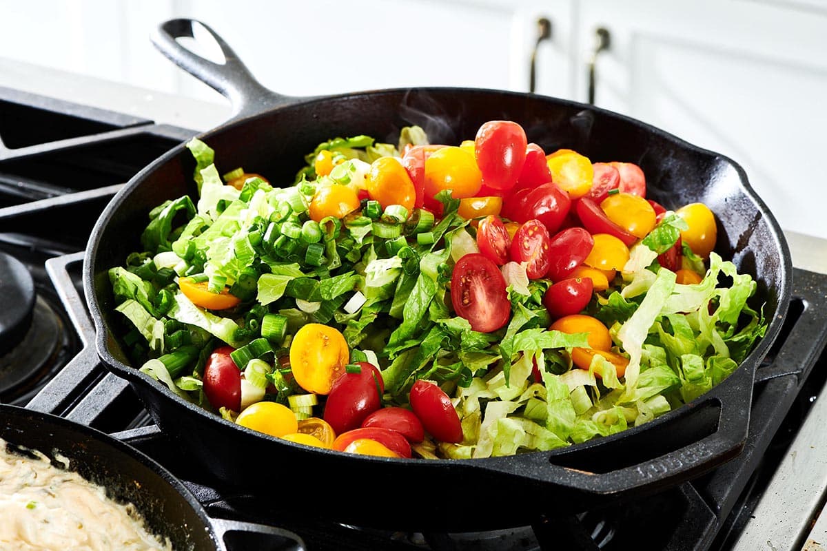 Tomatoes, lettuce, and scallions in a skillet.