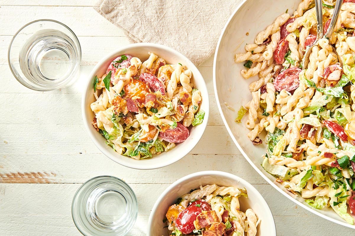 Bowls of BLT Pasta Salad on table with water glasses and napkin.