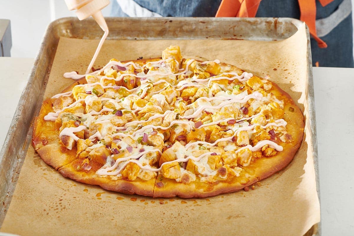 Woman drizzling sauce onto a Buffalo Chicken Pizza.