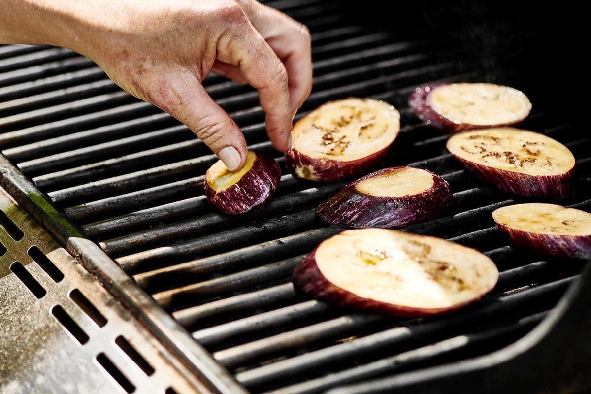 Placing oiled eggplant slices on hot grill.