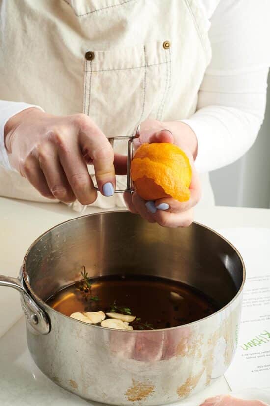 Woman peeling an orange into a pot of brine.
