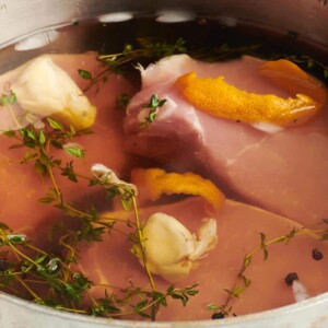 Pork chops floating in a pot of brine with thyme, orange peel, and garlic.