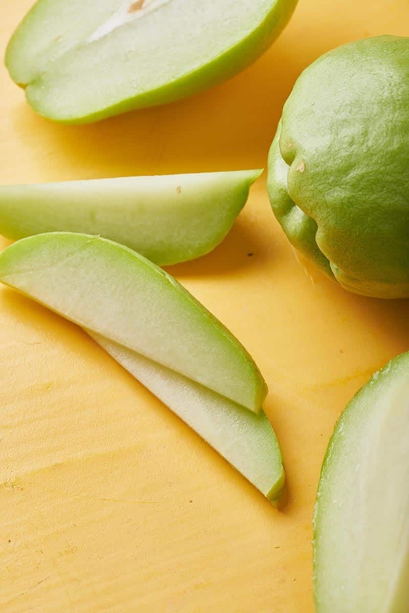 Whole and sliced fresh chayote on wood.