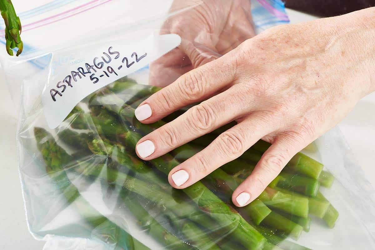 Woman placing blanched asparagus into labeled freezer bag.