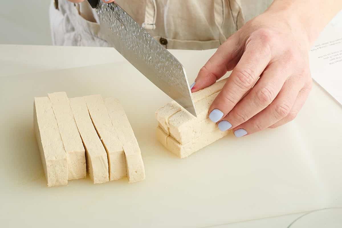Woman chopping tofu into cubes.