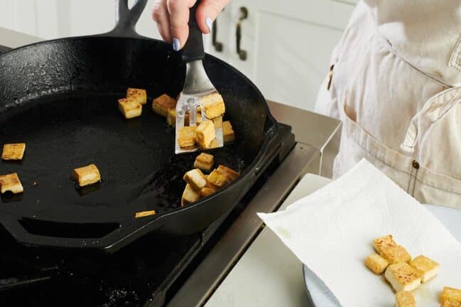 Spatula flipping cubes of tofu in a cast iron pan.