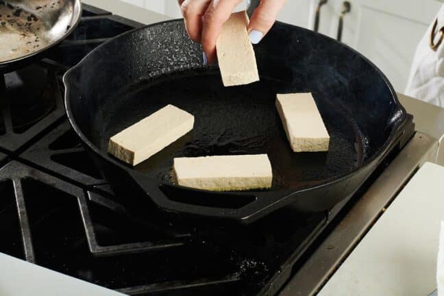 Woman placing tofu into a cast iron pan.