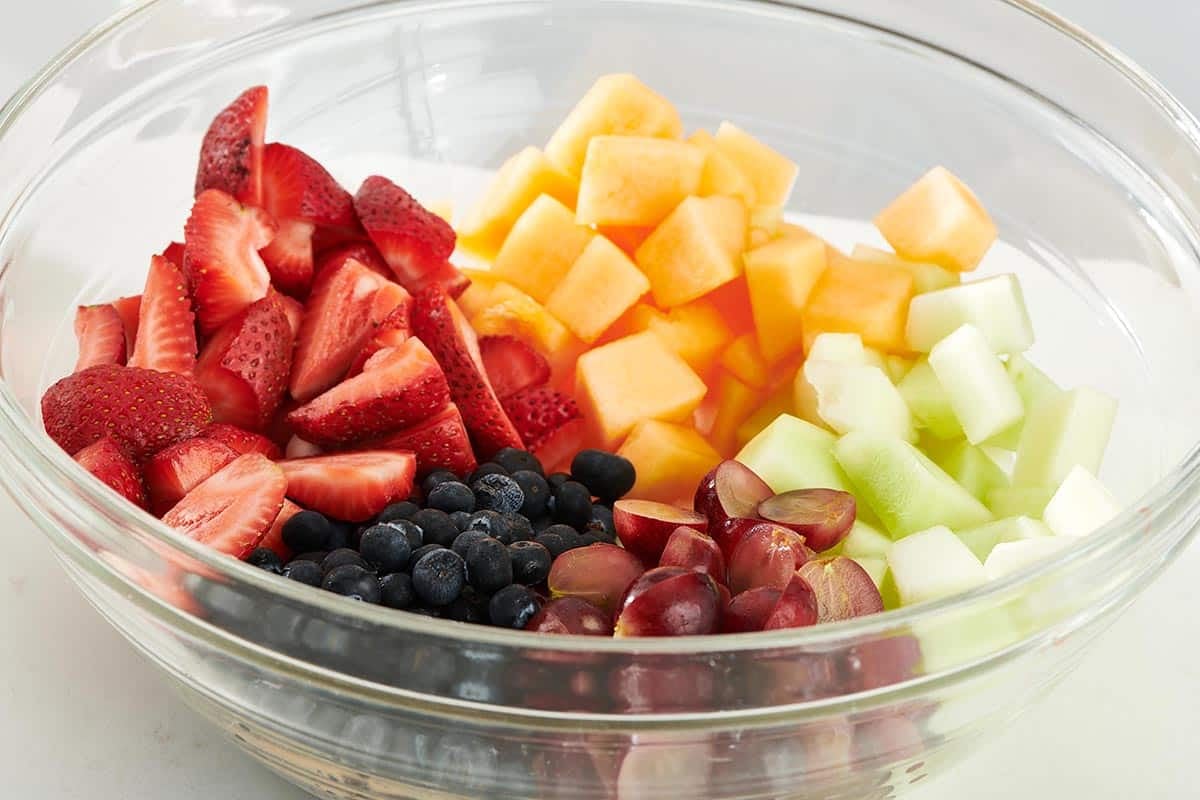 Colorful fruits, including strawberries, blueberries, and melon, unmixed in a glass bowl.