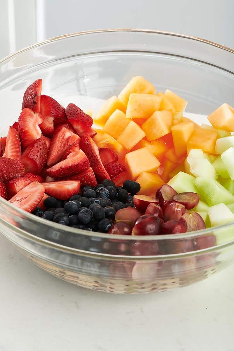 Strawberries, melon, grapes, and blueberries unmixed in a glass bowl.