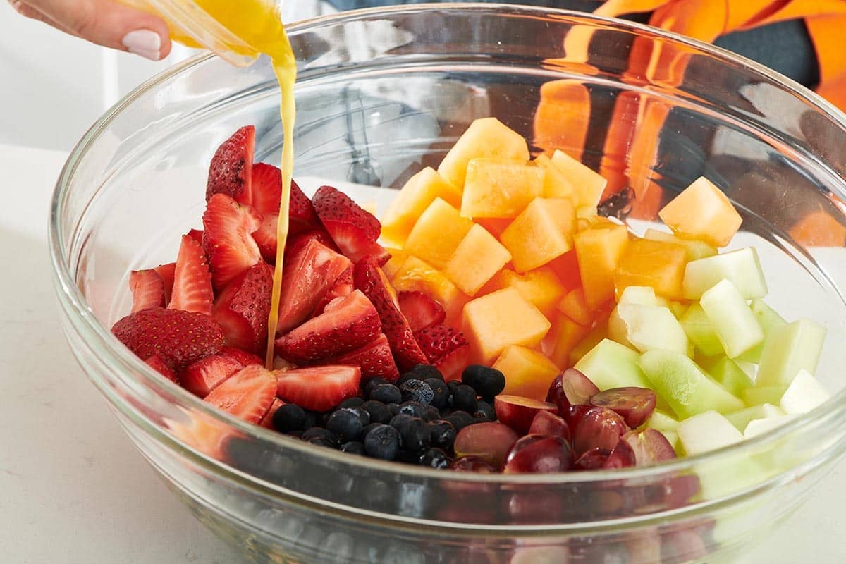 Dressing being poured into a bowl of unmixed fruit.