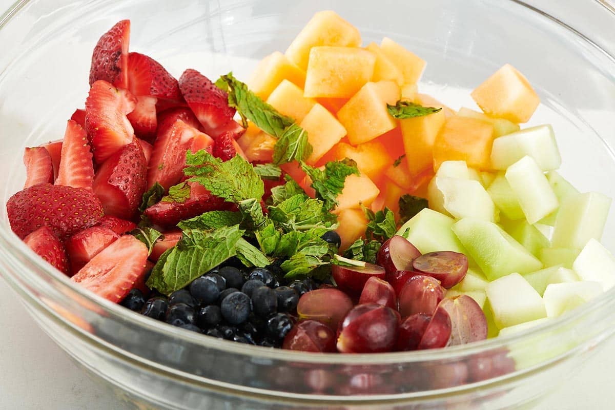 Mint on top of colorful fruit unmixed in a bowl.