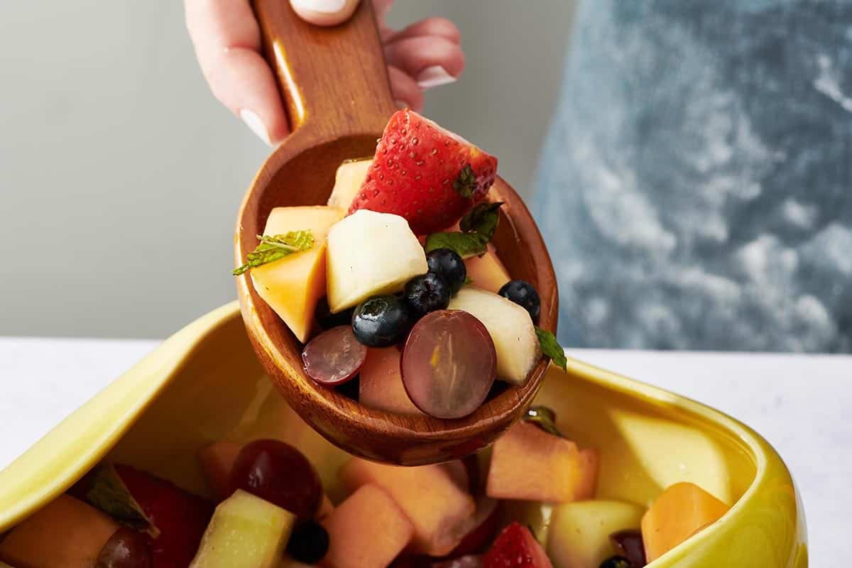 Wooden spoon with a scoop of fruit salad.