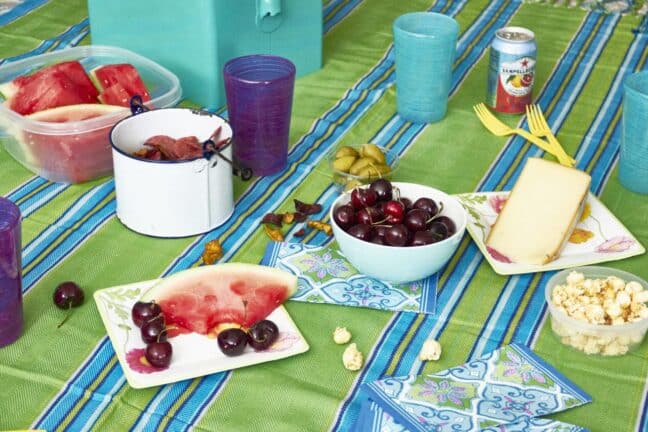 Table set with fruit, popcorn, cheese, and a colorful tablecloth.
