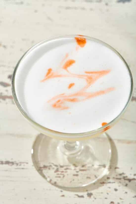 Pisco Sour in long-stemmed glass on a white, wooden table.