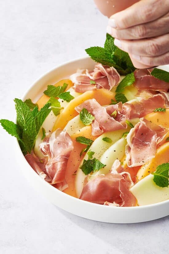 Woman grinding pepper onto a bowl of Prosciutto and Melon.