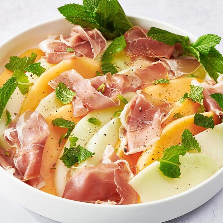 Bowl of Prosciutto and Melon topped with mint leaves and pepper.