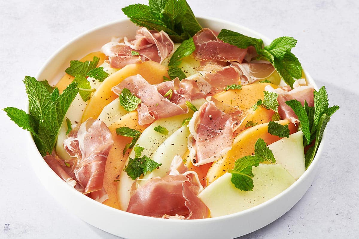 Bowl of Prosciutto and Melon topped with mint leaves and pepper.
