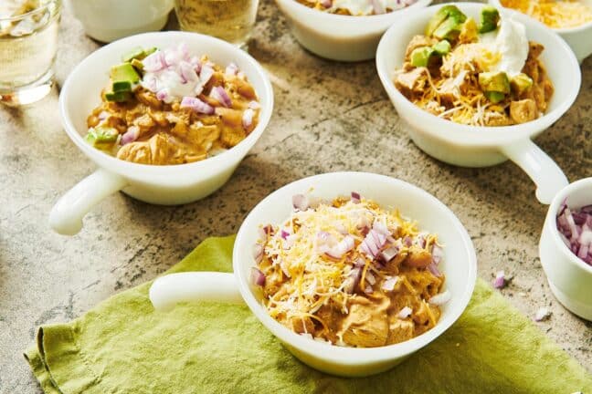 Bowls of White Chicken Chili with different toppings, including shredded cheese, avocado, and red onion.