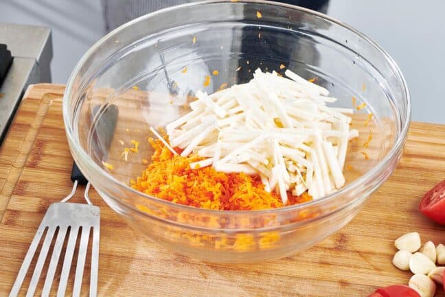 Glass bowl with shredded carrots and long slices of celeriac.