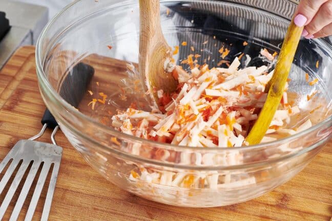 Wooden utensils tossing a bowl of Carrot Celeriac Remoulade.