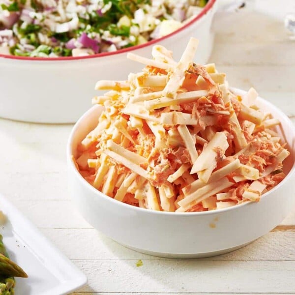 Heaping bowl of Carrot Celeriac Remoulade set on a white, wooden table.