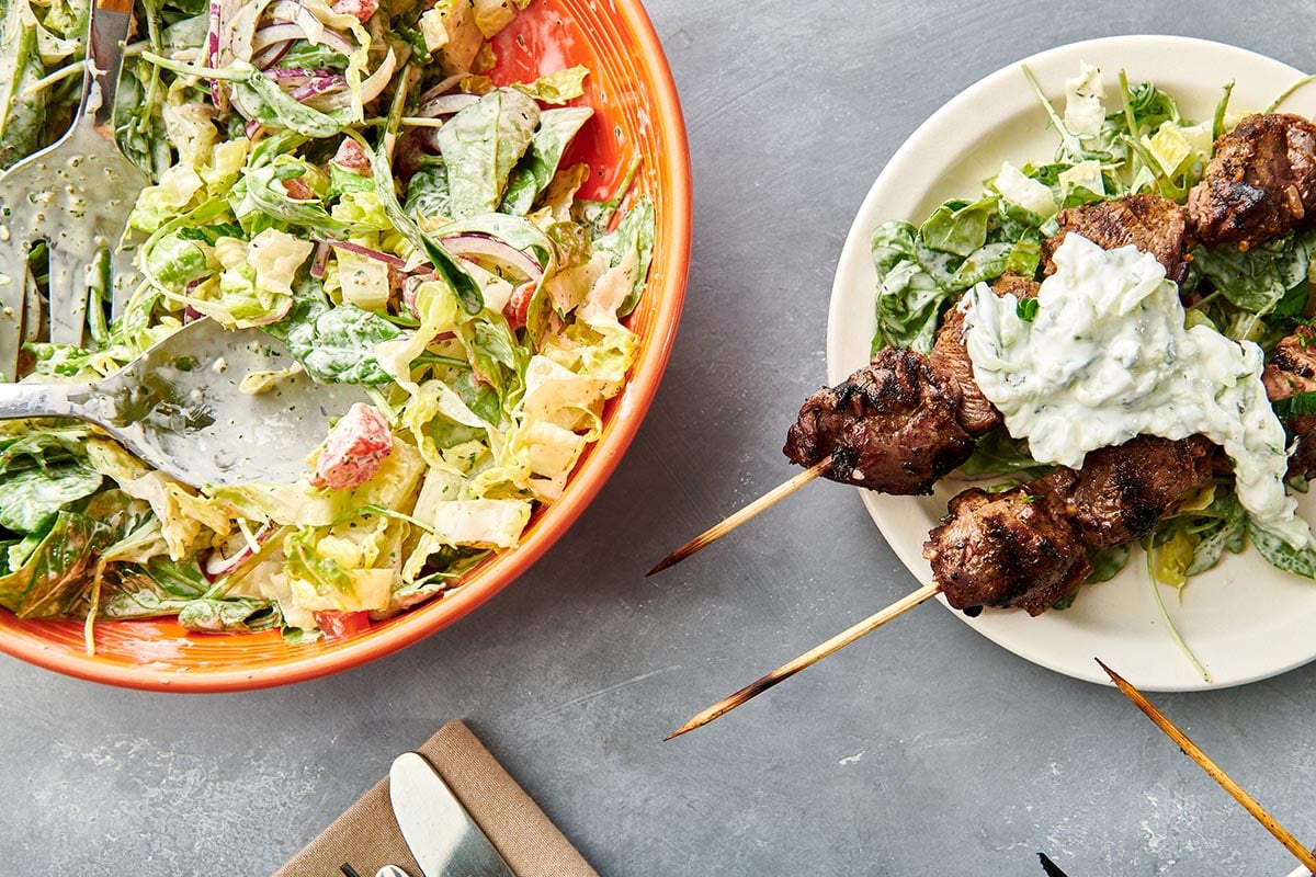 Greek Lamb Kebobs next to a bowl of salad.