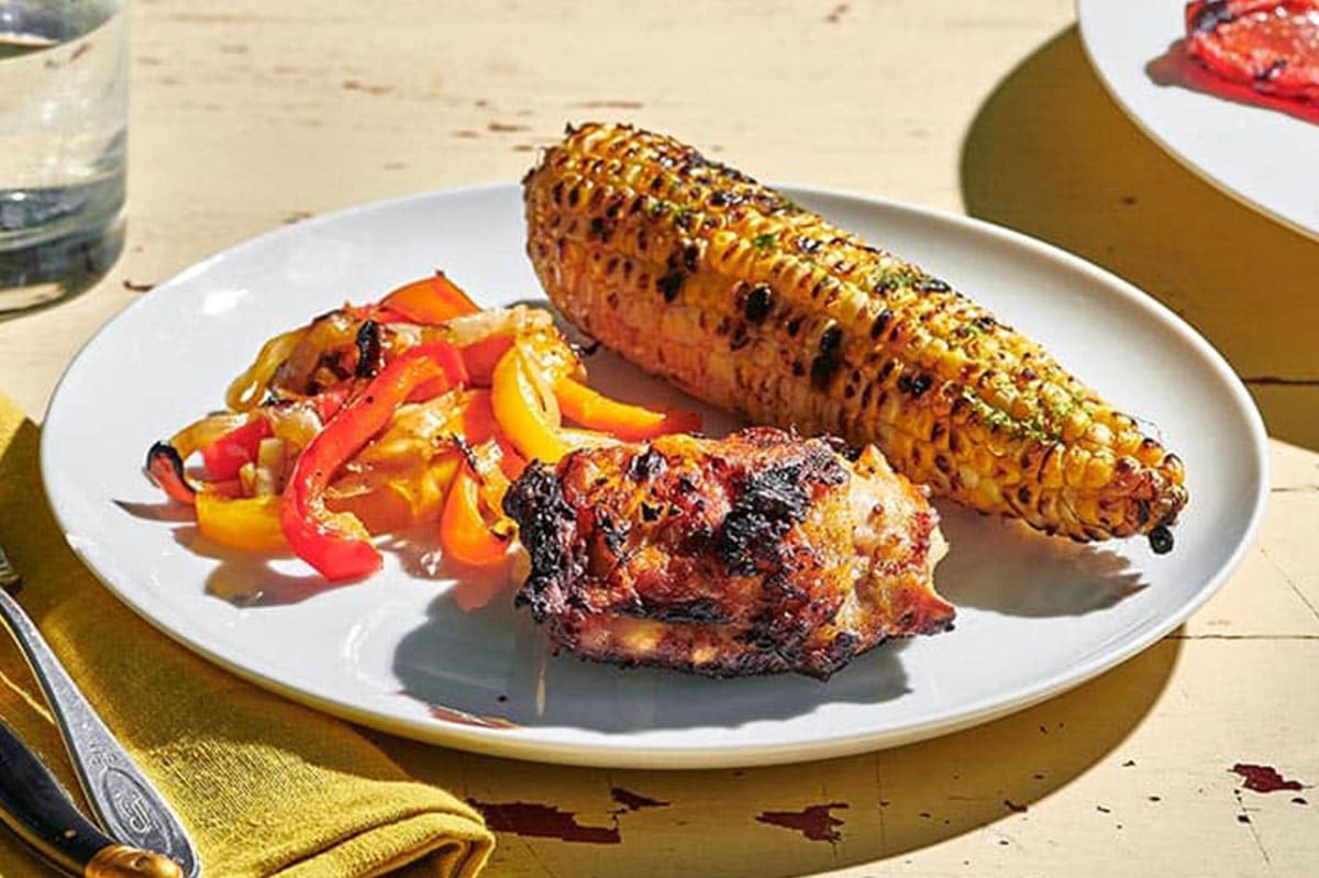 Grilled Chicken Thighs on a plate with corn and peppers set on an outdoor table.