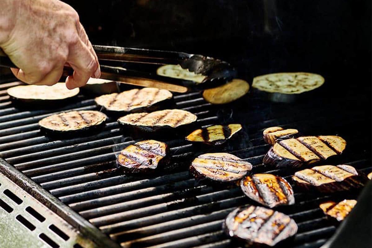 Flipping grilled eggplant with barbecue tongs.