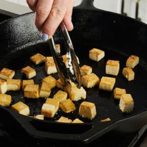 Frying tofu cubes in skillet on stove.